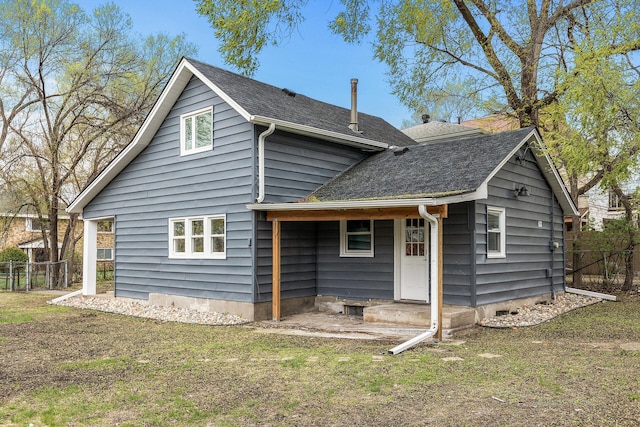 rear view of house with a yard, roof with shingles, and fence