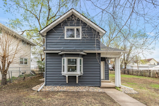 rear view of house with roof with shingles, covered porch, and fence