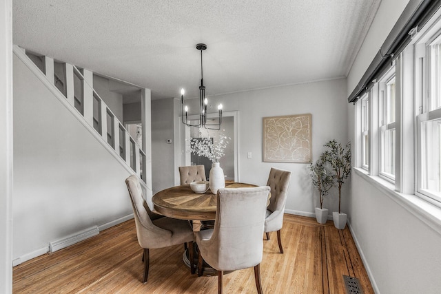 dining area with an inviting chandelier, a textured ceiling, light wood-style flooring, and visible vents