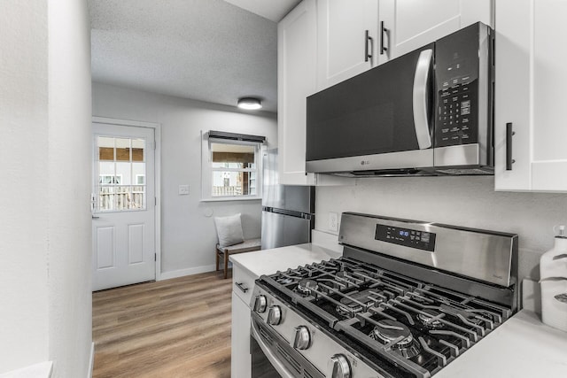 kitchen with appliances with stainless steel finishes, white cabinetry, baseboards, light countertops, and light wood-style floors