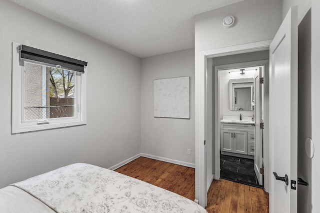 bedroom featuring a sink, ensuite bathroom, baseboards, and wood finished floors