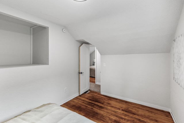 unfurnished bedroom featuring baseboards, wood finished floors, and vaulted ceiling