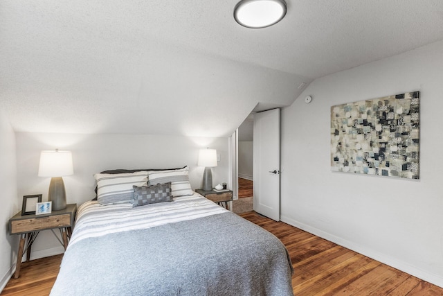 bedroom featuring a textured ceiling, vaulted ceiling, wood finished floors, and baseboards