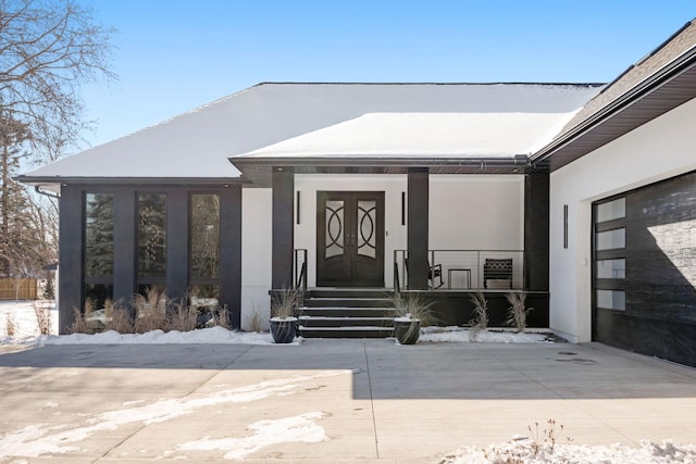 snow covered property entrance featuring covered porch, driveway, and stucco siding