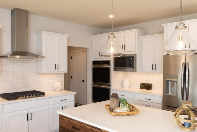 kitchen with stainless steel appliances, tasteful backsplash, wall chimney exhaust hood, decorative light fixtures, and white cabinets