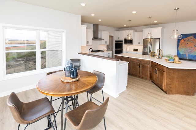 kitchen featuring stainless steel appliances, wall chimney range hood, white cabinetry, and pendant lighting