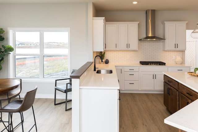 kitchen featuring light hardwood / wood-style floors, wall chimney exhaust hood, sink, tasteful backsplash, and white cabinetry