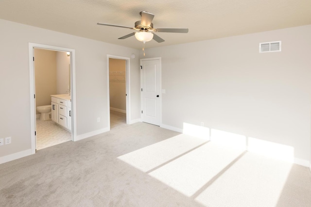 unfurnished bedroom with ensuite bath, light carpet, ceiling fan, a closet, and a walk in closet