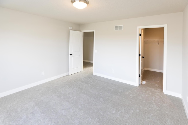 unfurnished bedroom featuring a closet, a walk in closet, and light colored carpet