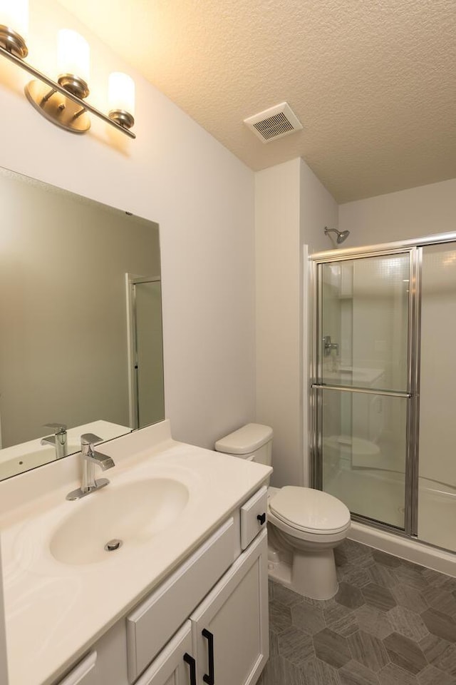 bathroom featuring a shower with door, vanity, toilet, and a textured ceiling