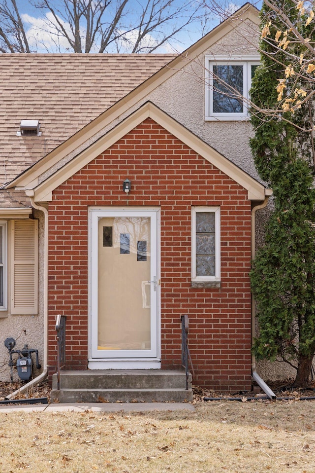view of exterior entry featuring brick siding and roof with shingles