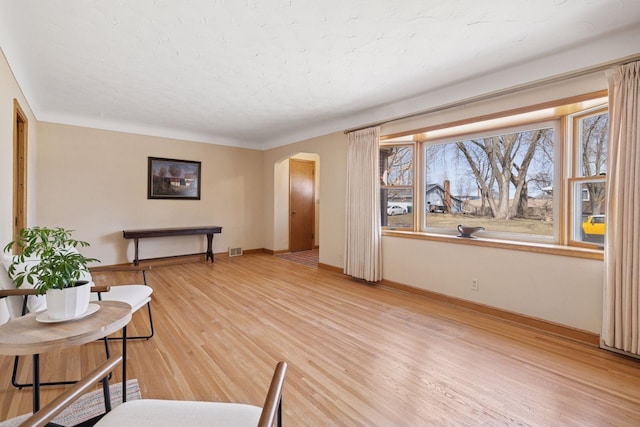 sitting room with baseboards, arched walkways, and light wood-type flooring