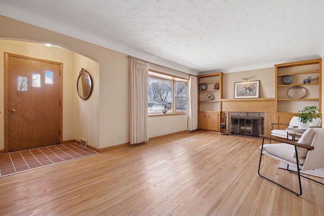 foyer with baseboards, a fireplace with flush hearth, light wood-style floors, and a textured ceiling