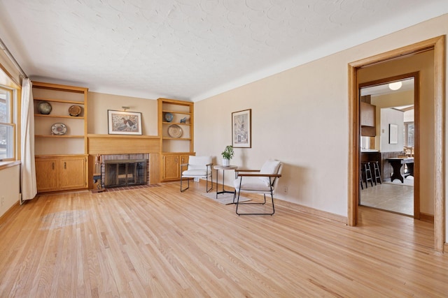 sitting room with a glass covered fireplace, baseboards, and light wood-style flooring