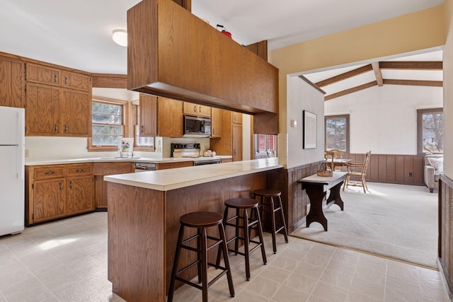 kitchen featuring white appliances, brown cabinetry, a wainscoted wall, vaulted ceiling with beams, and light countertops