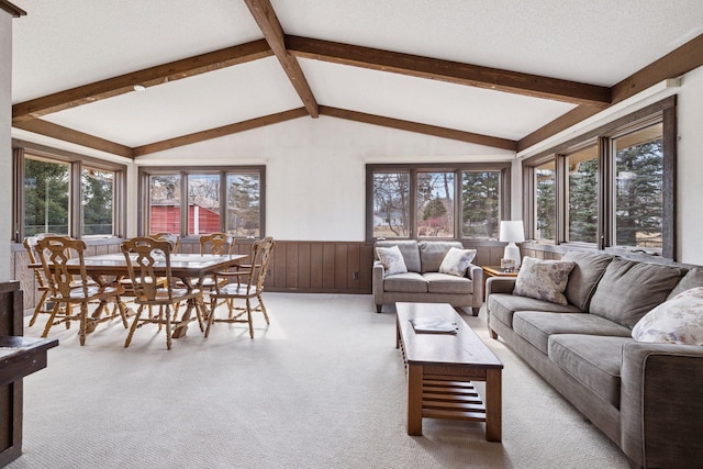 carpeted living area featuring a textured ceiling, vaulted ceiling with beams, and wainscoting