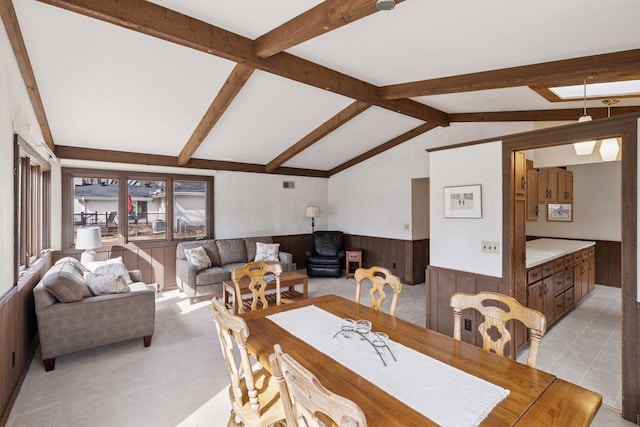 dining area featuring lofted ceiling with beams, wooden walls, light tile patterned floors, and a wainscoted wall