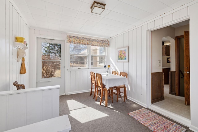 carpeted dining room with arched walkways and baseboards
