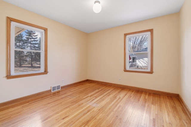 unfurnished room with light wood finished floors, visible vents, and baseboards
