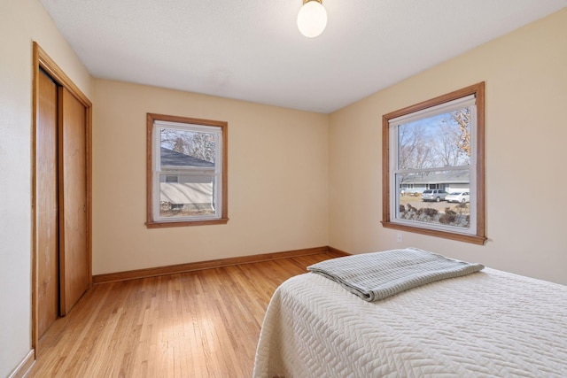 bedroom with multiple windows, light wood-style flooring, and baseboards