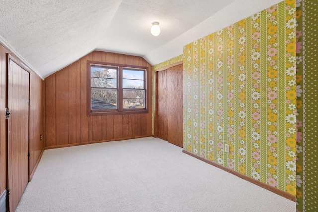 bonus room featuring a textured ceiling, baseboards, wooden walls, carpet flooring, and lofted ceiling