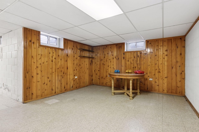 below grade area featuring tile patterned floors, a drop ceiling, baseboards, and wooden walls