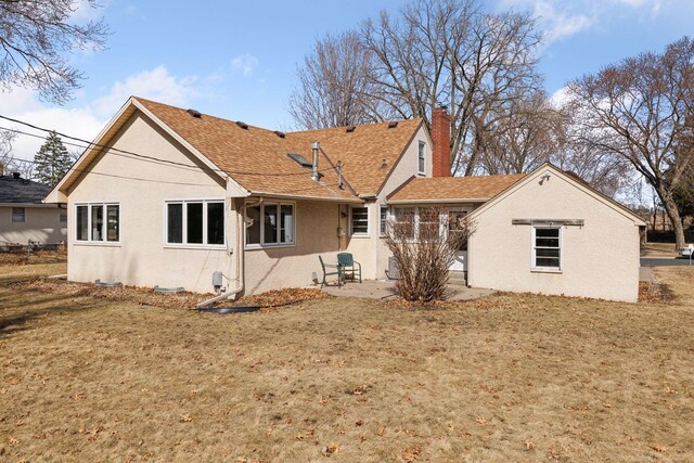 rear view of house featuring roof with shingles, stucco siding, a lawn, a chimney, and a patio area