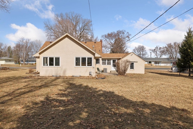 back of house with stucco siding, a chimney, and a lawn