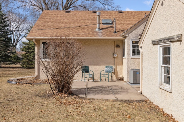 rear view of property featuring stucco siding, central air condition unit, roof with shingles, and a patio area