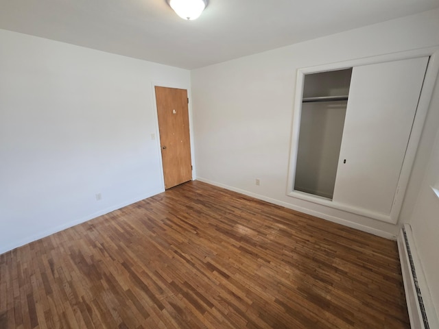 unfurnished bedroom with dark hardwood / wood-style floors, a closet, and a baseboard heating unit