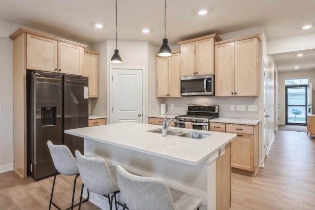 kitchen with hanging light fixtures, sink, light brown cabinets, light wood-type flooring, and appliances with stainless steel finishes