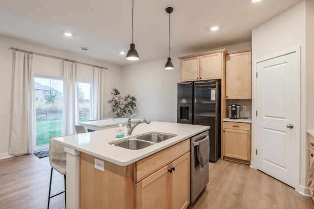 kitchen featuring sink, light brown cabinetry, hanging light fixtures, light hardwood / wood-style flooring, and dishwasher