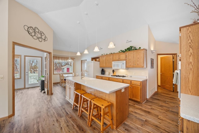 kitchen with white appliances, a kitchen island with sink, sink, wood-type flooring, and decorative light fixtures