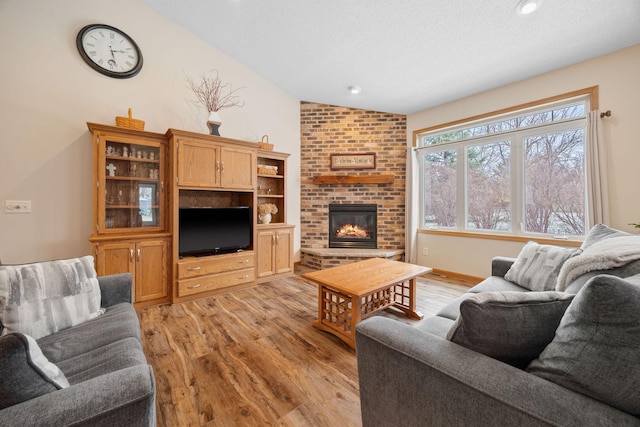 living room with a textured ceiling, light hardwood / wood-style flooring, lofted ceiling, and a brick fireplace