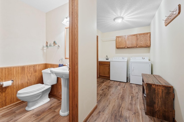 laundry room featuring a textured ceiling, wooden walls, sink, independent washer and dryer, and light hardwood / wood-style floors