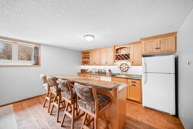 kitchen with white appliances, light wood-type flooring, a textured ceiling, light brown cabinetry, and a breakfast bar area