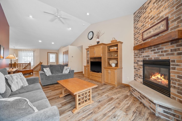 living room featuring a fireplace, light wood-type flooring, ceiling fan, and lofted ceiling