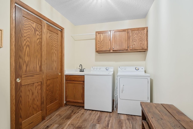 clothes washing area featuring cabinets, light wood-type flooring, a textured ceiling, and washing machine and clothes dryer