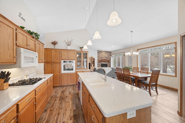 kitchen featuring a center island with sink, light countertops, light wood-style flooring, white appliances, and a sink