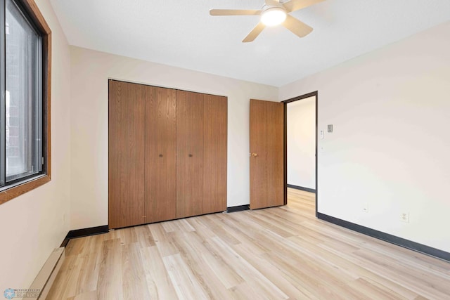 unfurnished bedroom featuring ceiling fan, a baseboard radiator, a closet, and light wood-type flooring