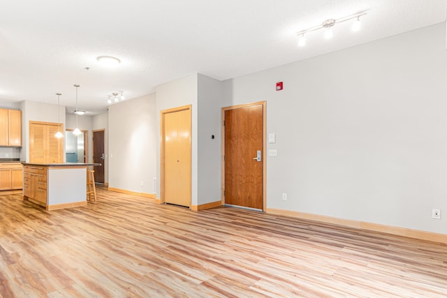 interior space with a kitchen breakfast bar, light brown cabinets, pendant lighting, a center island, and light wood-type flooring