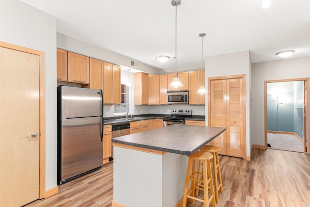 kitchen with stainless steel appliances, a center island, hanging light fixtures, a kitchen breakfast bar, and light hardwood / wood-style flooring