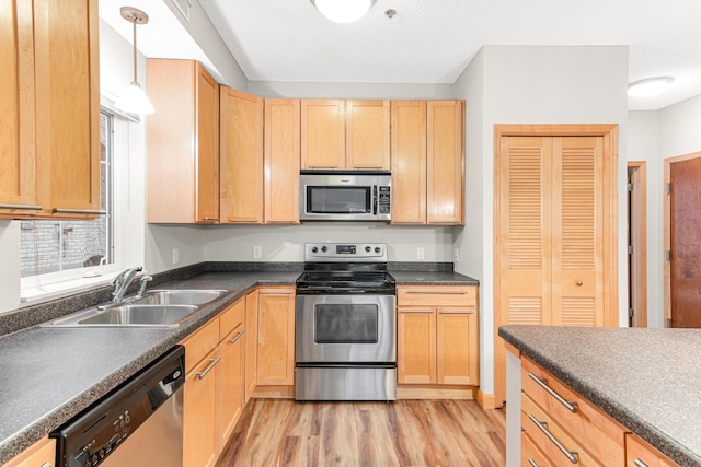 kitchen with light wood-type flooring, appliances with stainless steel finishes, light brown cabinetry, pendant lighting, and sink