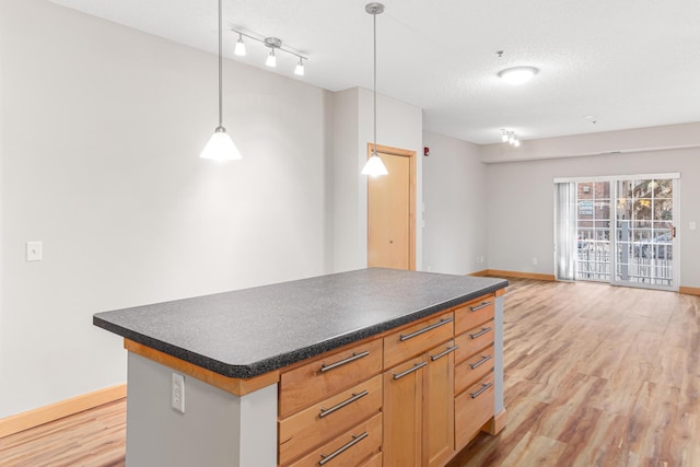 kitchen featuring a textured ceiling, light wood-type flooring, a kitchen island, and decorative light fixtures