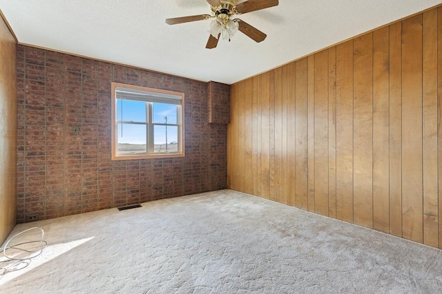 unfurnished room featuring wooden walls, carpet, and ceiling fan