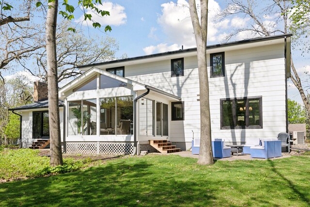 rear view of property featuring entry steps, a sunroom, a lawn, and a chimney