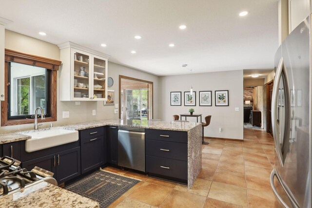 kitchen featuring glass insert cabinets, appliances with stainless steel finishes, a peninsula, white cabinetry, and a sink