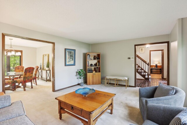 living area with a chandelier, light carpet, baseboards, and stairs