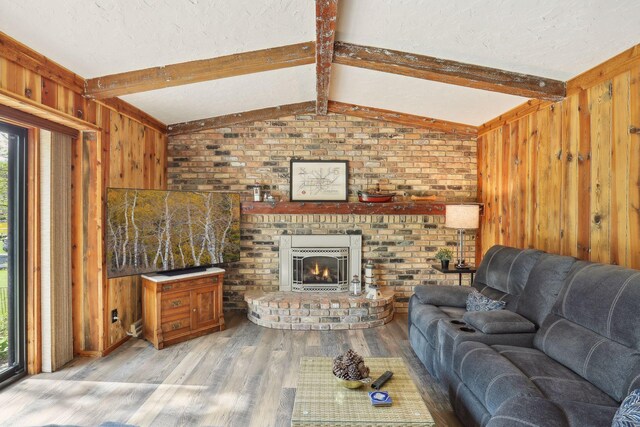 living area with light wood-style floors, lofted ceiling with beams, a textured ceiling, wood walls, and a fireplace