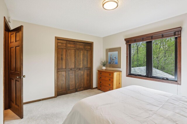 bedroom featuring a closet, light colored carpet, a textured ceiling, and baseboards